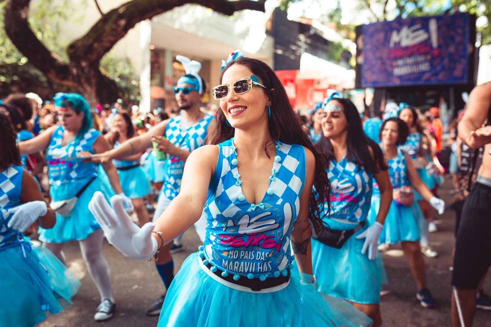 Foliona da ala de dança do Me Deixe! sorrindo no desfile de 2025, de óculos escuros e luva branca